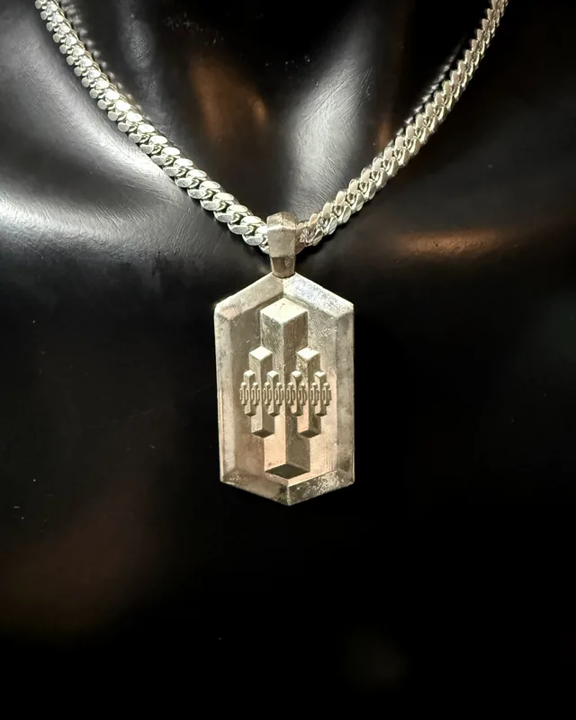 A silver pendant with stepped art deco towers rising from its face